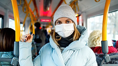 Frau steht im Bus mit Maske und Mütze