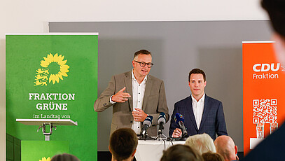 Andreas Schwarz und Manuel Hagel vor Journalist*innen während der Halbzeit-Pressekonferenz 2023.