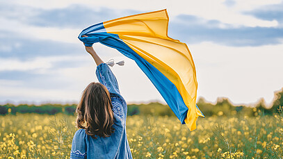 Frau hält Ukrainische Flagge in die Luft, während sie in einem Blumenfeld steht.