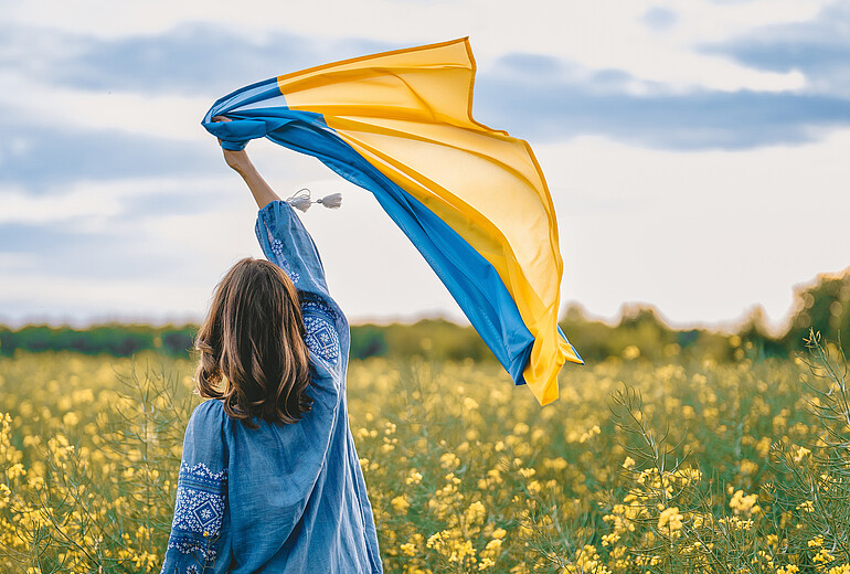 Frau hält Ukrainische Flagge in die Luft, während sie in einem Blumenfeld steht.