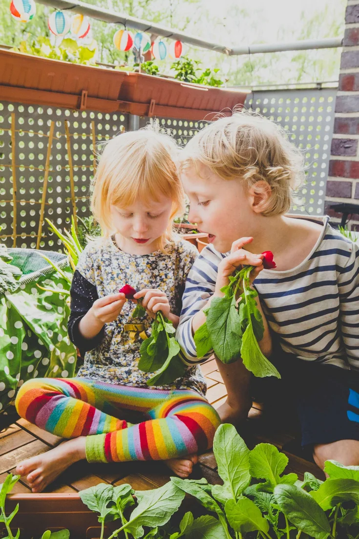 Zwei Kinder sitzen auf dem Balkon und bestaunen Radieschen.