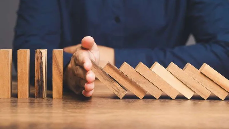 Eine Hand stoppt die umkippenden Dominosteine aus Holz