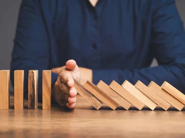 Eine Hand stoppt die umkippenden Dominosteine aus Holz