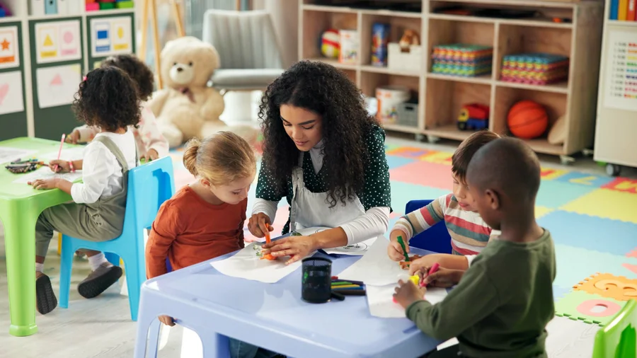 Kinder und Erzieherin malen gemeinsam in einer fröhlichen, bunten Kita-Umgebung.