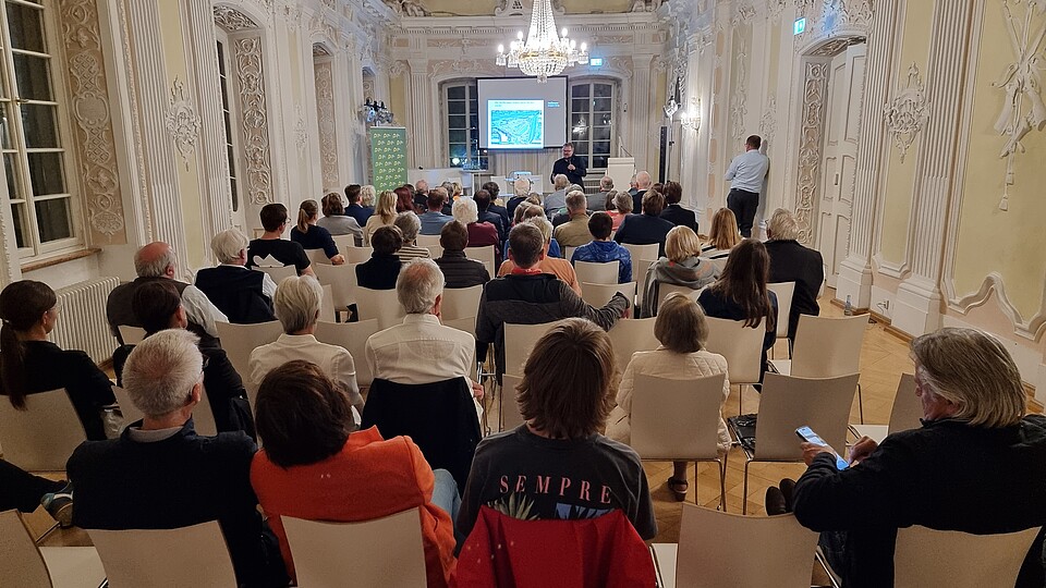 100 Menschen sitzen in einem altehrwürdigen Schießhaus