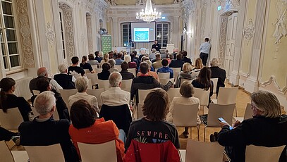 100 Menschen sitzen in einem altehrwürdigen Schießhaus