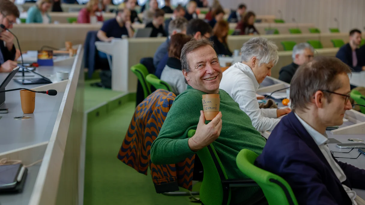 Unser Abgeordneter Thomas Marwein hält einen Kaffeebecher in die Kamera und strahlt.