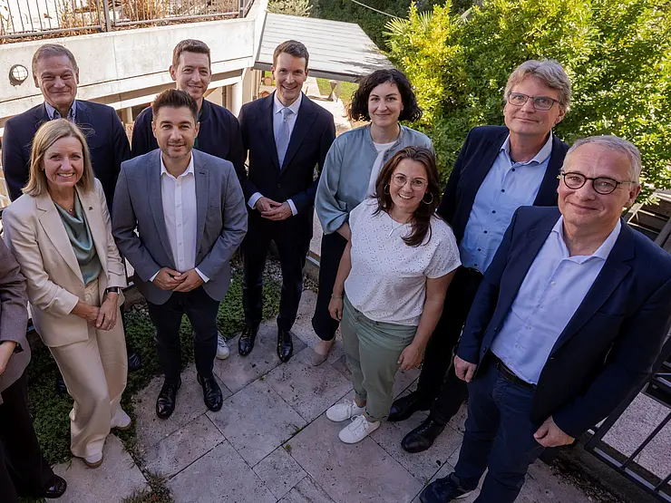 Eine Gruppe von Menschen steht auf einer Terrasse und lächelt in die Kamera