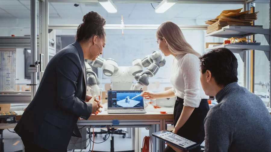 Diverses Team von Studierenden arbeiten an der Foschung zur Robotik in einem technischen Labor. Im Hintergrund ist der Roboter zu erkennen. 