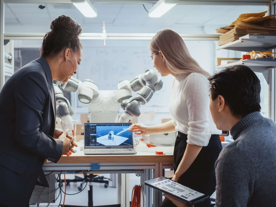 Diverses Team von Studierenden arbeiten an der Foschung zur Robotik in einem technischen Labor. Im Hintergrund ist der Roboter zu erkennen. 