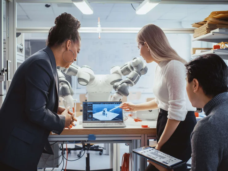 ForschungRoboter_544381837 Diverses Team von Studierenden arbeiten an der Foschung zur Robotik in einem technischen Labor. Im Hintergrund ist der Roboter zu erkennen.