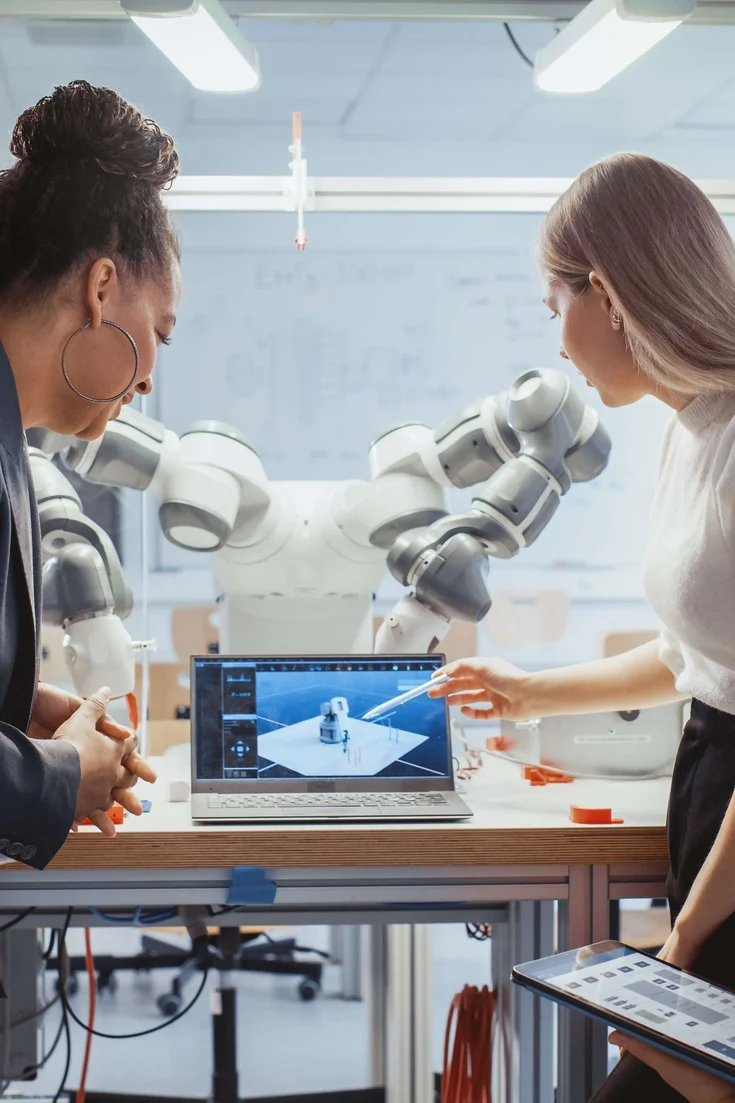 Diverses Team von Studierenden arbeiten an der Foschung zur Robotik in einem technischen Labor. Im Hintergrund ist der Roboter zu erkennen. 