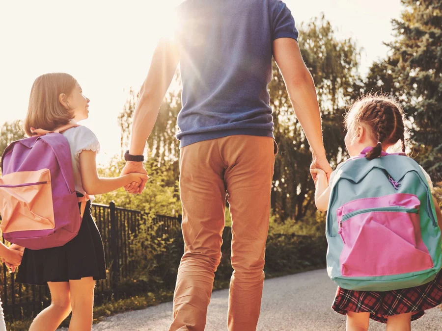 Erwachsener bringt drei Kinder zu Fuß zur Schule