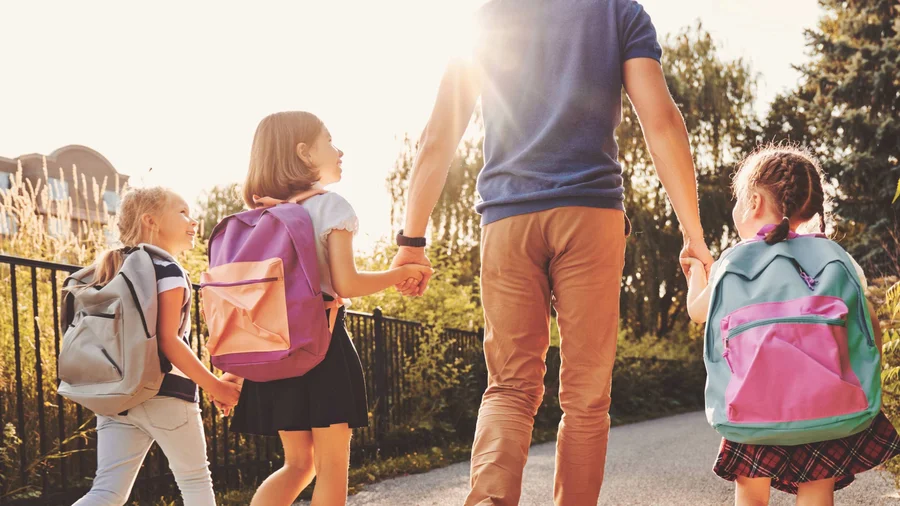 Erwachsener bringt drei Kinder zu Fuß zur Schule
