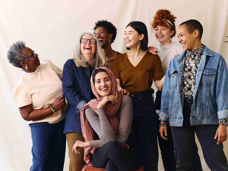 Eine Gruppe von PoC-Frauen stehe vor einem hellen Vorhang und haben Spaß