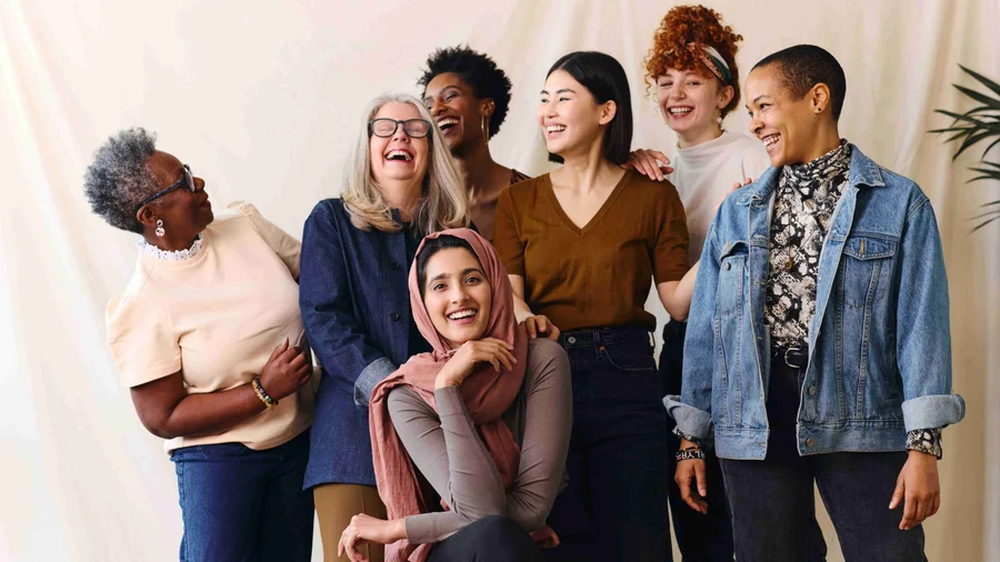 Eine Gruppe von PoC-Frauen stehe vor einem hellen Vorhang und haben Spaß