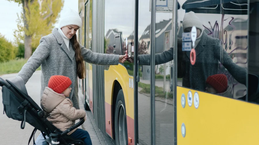 Eine weibliche gelesene Person möchte mit dem Kinderwagen in einen Bus einsteigen.