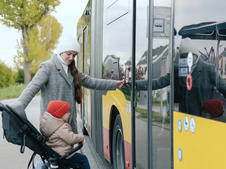 Eine weibliche gelesene Person möchte mit dem Kinderwagen in einen Bus einsteigen.