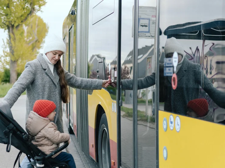 Eine weibliche gelesene Person möchte mit dem Kinderwagen in einen Bus einsteigen.