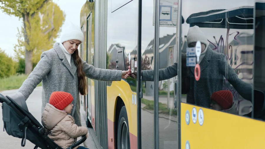 Eine weibliche gelesene Person möchte mit dem Kinderwagen in einen Bus einsteigen.