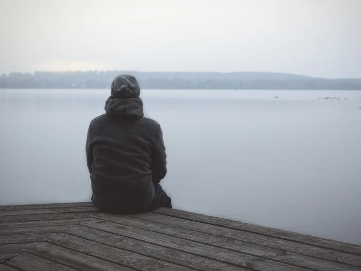 Mann sitzt allein an einem Steg am See.