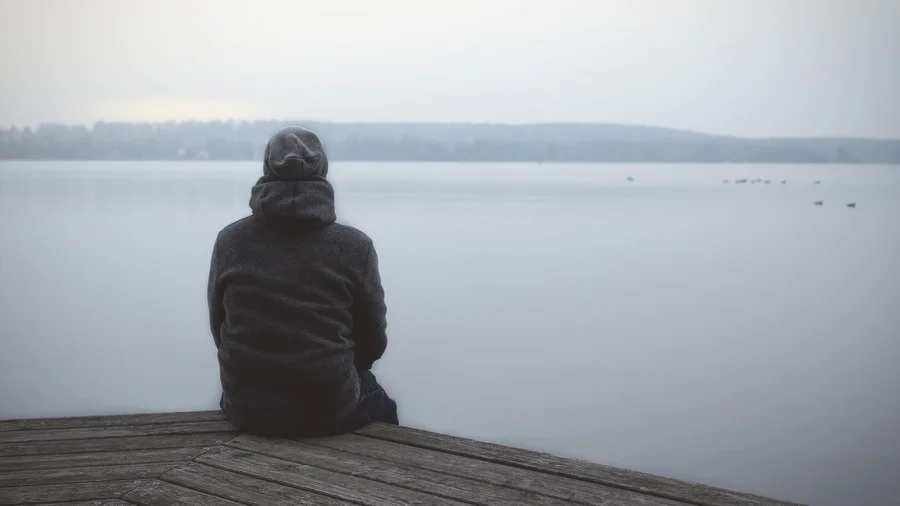 Mann sitzt allein an einem Steg am See.