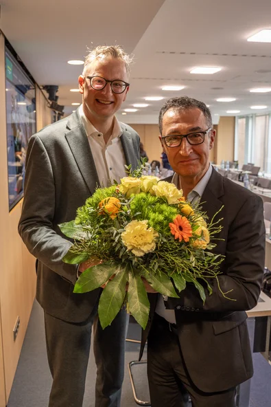 Cem Özdemir erhält von Andreas Schwarz einen Blumenstrauß und freut sich.