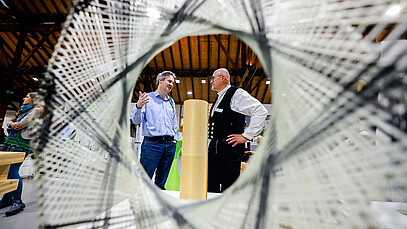 Das Bild zeigt ein robotisch gefertiges, ultraleichtes Bauteil am Stand des Exzellenzclusters IntCDC der Universität Stuttgart mit zwei Besuchern der Veranstaltung.