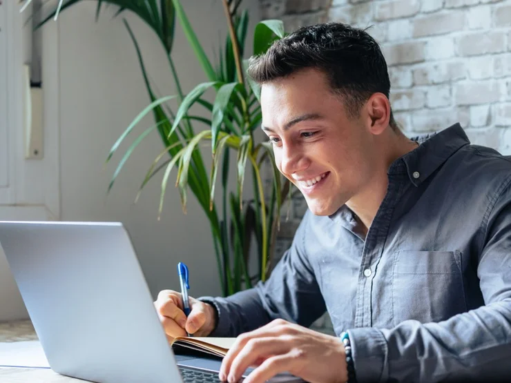 Junger Mann sitzt vor einem Laptop und lacht
