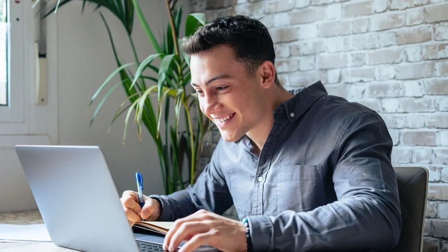 Junger Mann sitzt vor einem Laptop und lacht