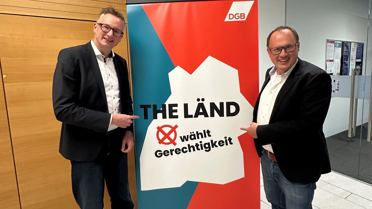 Fraktionsvorsitzende der Grünen, Andreas Schwarz, und der Vorsitzende des DGB Baden-Württemberg, Kai Burmeister, stehen vor einem Plakat von bwgerecht.jetzt