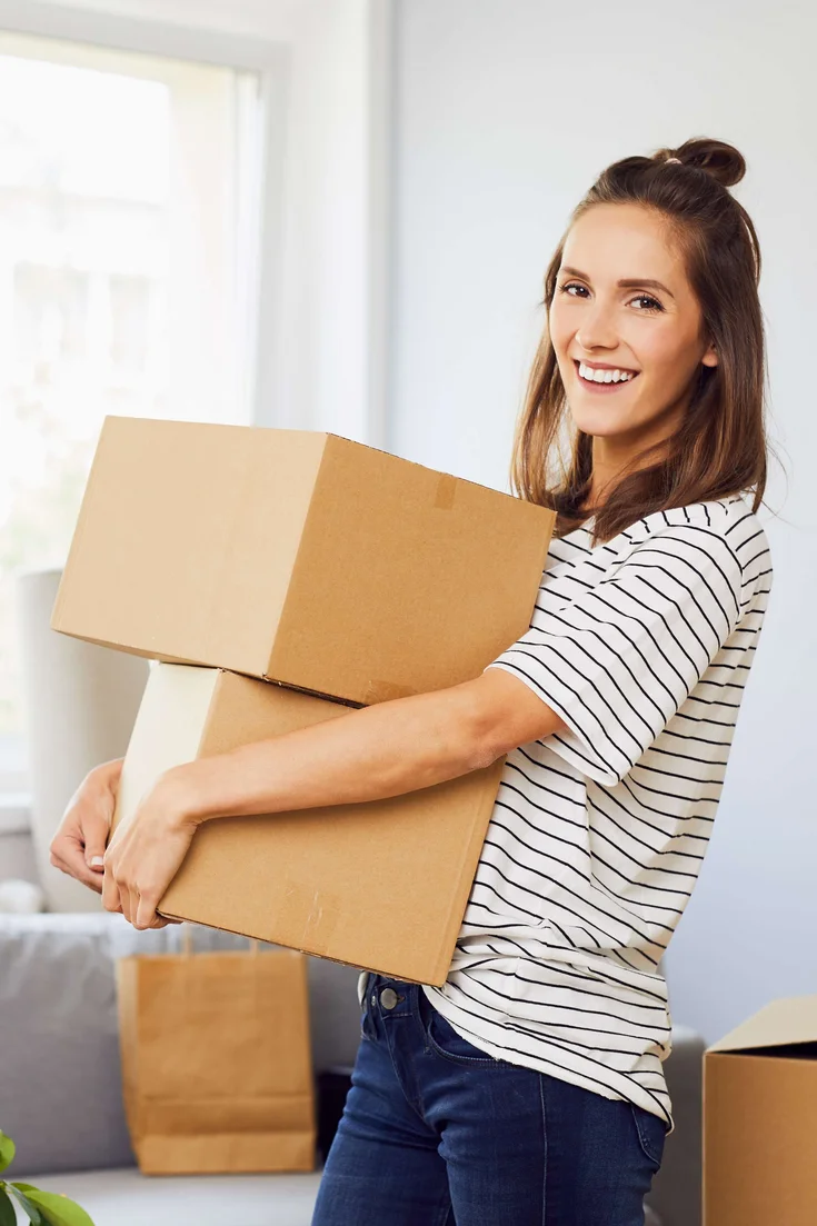 Junge Frau zieht in eine Wohnung ein und hält zwei Umzugkartons in der Hand.