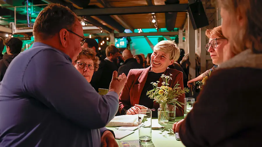 An einem Stehtisch stehen Menschen, die sich miteinander unterhalten.