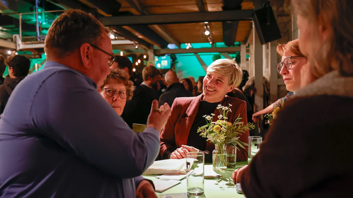 An einem Stehtisch stehen Menschen, die sich miteinander unterhalten.