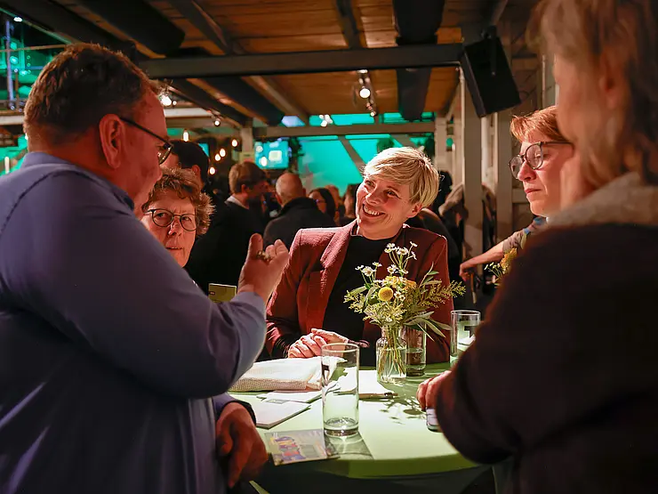 An einem Stehtisch stehen Menschen, die sich miteinander unterhalten.