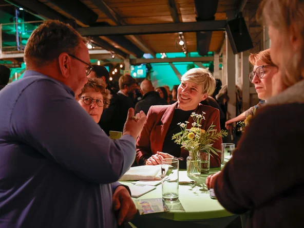 An einem Stehtisch stehen Menschen, die sich miteinander unterhalten.