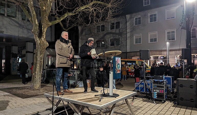 Zwei Männer stehen auf einer Bühne und halten eine Rede.