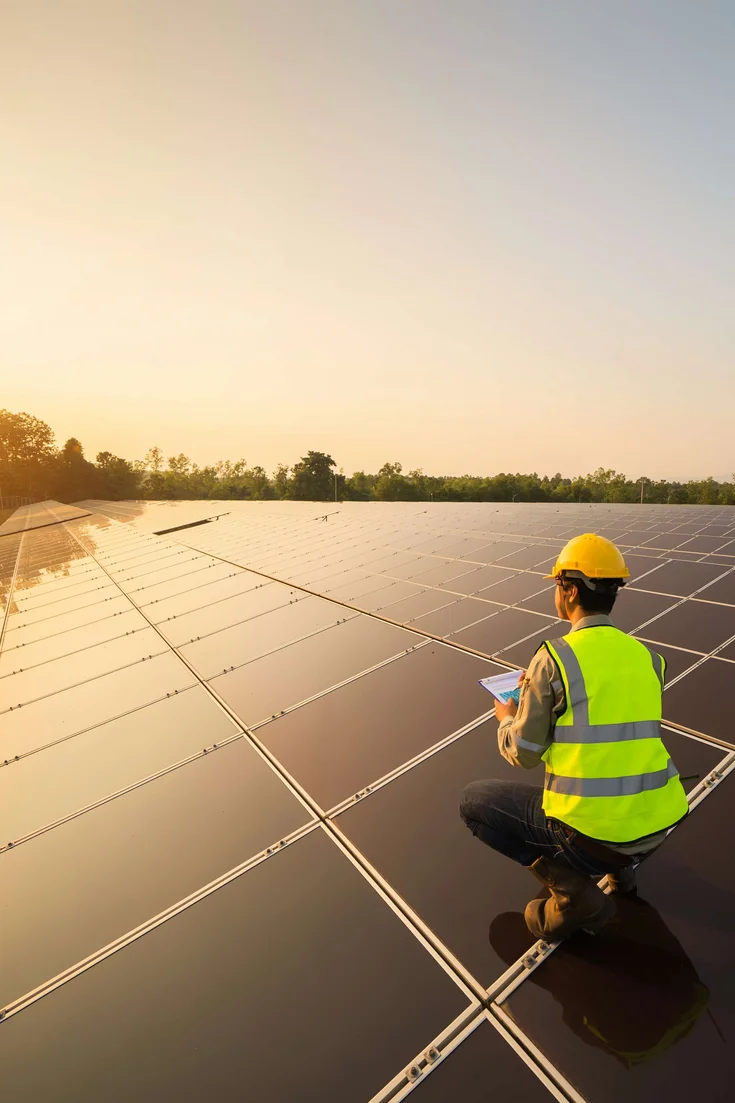 Ein:e Ingeneur:in arbeitet auf einer Fläche von Solaranlagen und blickt in den Sonnenuntergang.