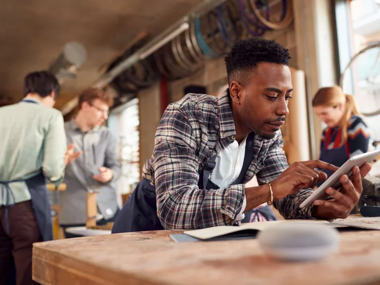 Bambusfahrradwerkstatt_345561413 Mann guckt konzentriert auf sein Tablet in einem StartUp-Farradladen, das Bambus-Räder entwickelt.